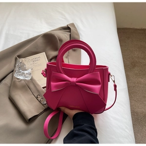 Close-up of rose pink matte leather handbag featuring a large bow and metallic logo