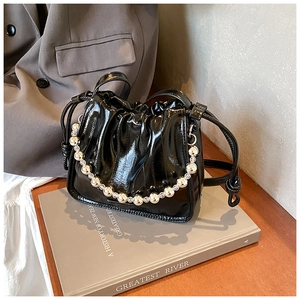 Detail of black patent leather bucket bag with decorative beads and pleated texture