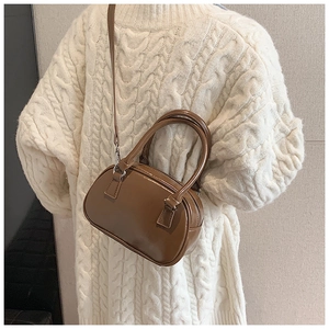 Dettaglio borsa bowling in pelle verniciata marrone scuro indossata con un maglione