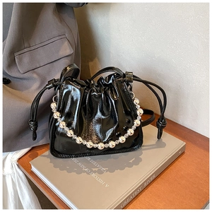 Detail of black glossy drawstring bucket bag with decorative silver and clear bead chain
