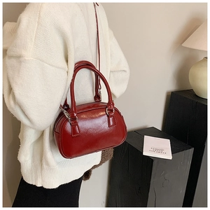 Dettaglio di una borsa Boston rosso vino lucida con doppi manici e tracolla argentata