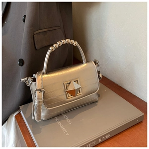 Sac argenté avec poignée en perles et fermoir pyramide doré sur des livres