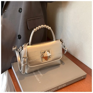 Détail du sac à main en cuir métallisé avec poignée perlée et boucle pyramide en métal