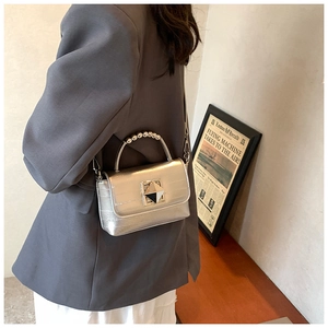 Détail du sac à main argenté avec poignée perlée et boucle métallique géométrique décorative