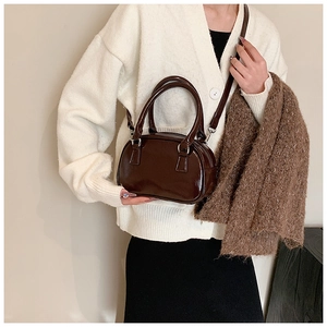 Dettaglio borsa bowling in pelle marrone scuro lucida con manici tondi e tracolla