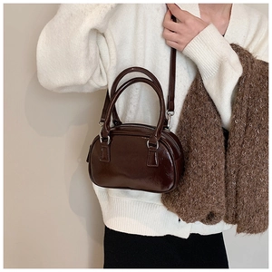 Dettaglio borsa bowling vintage in pelle lucida marrone scuro indossata con cardigan bianco