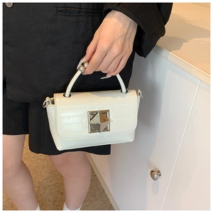 Gros plan d'un sac carré en cuir verni blanc avec boucle métallique porté par un modèle