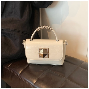 Détail du sac crème à motif crocodile avec poignée en perles et fermoir métallique carré