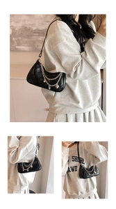 Detail of black quilted shoulder bag with silver chain heart charms on female model