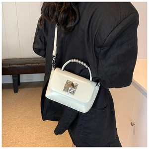 Détail d'un sac à main crème avec un fermoir en métal et une poignée à perles décorative