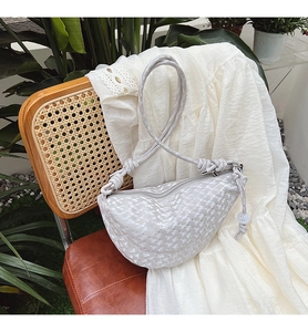 Détail du sac croissant gris clair avec jacquard texturé et sangle nouée sur chaise