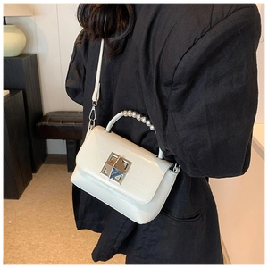 Détail du sac blanc motif croco avec boucle argentée et poignée perlée sur costume noir