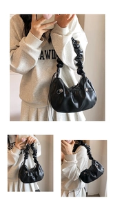 Detail of black dumpling bag featuring pleated handles and decorative silver buckles