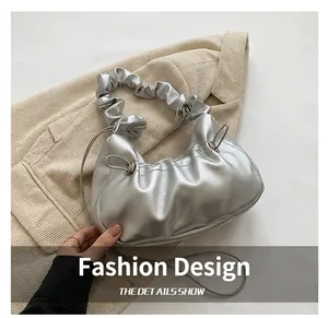Close-up of a silver pleated dumpling bag with textured handle on beige fabric