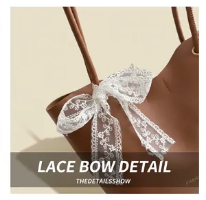 Detail of a brown leather tote with a large white lace bow and gold stamped lettering
