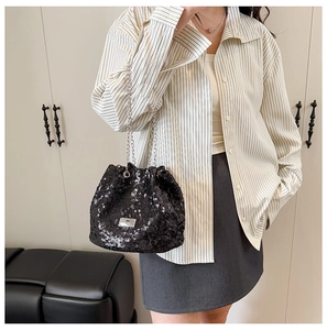 Detail of black sequined bucket bag with silver chain strap shown on a model