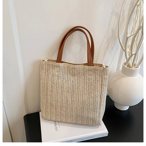 Detail of hand-woven beige straw tote bag with premium brown leather handles on books