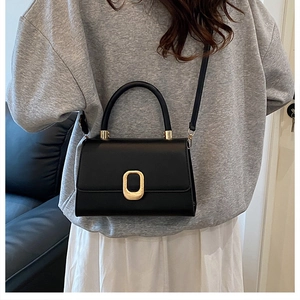 Close-up of minimalist black leather crossbody bag featuring a golden oval metal buckle