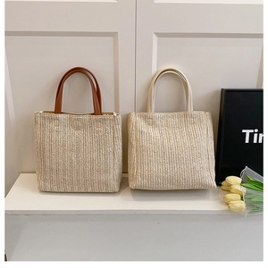 Détail de sacs fourre-tout tissés avec poignées marron et blanches sur table blanche