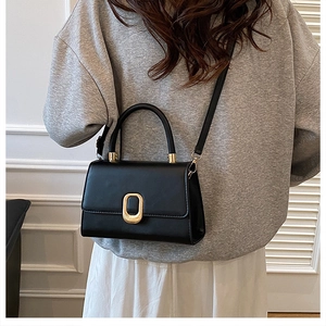 Detail of minimalist black crossbody bag with gold oval buckle and elegant top handle
