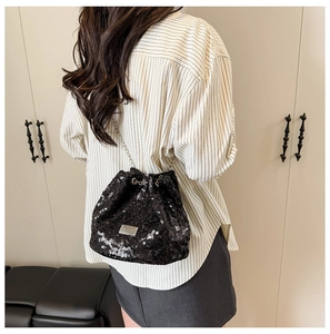 Detail of black sequined bucket bag with metal chain strap and drawstring closure worn by model