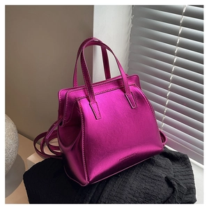 Detail of rose red metallic handbag with dual handles and adjustable shoulder strap