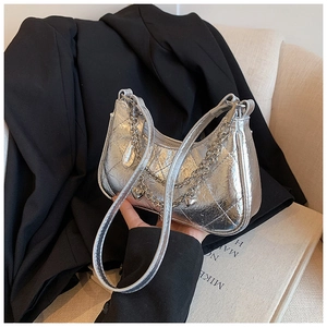 Close-up of quilted silver metallic shoulder bag with heart charm chain on a black blazer