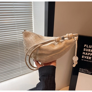 Detail of creamy white crescent bag featuring scale texture and knotted strap accents