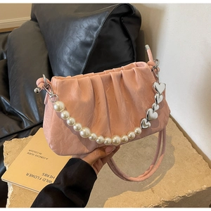 Close-up of pink pleated cloud bag with elegant pearl and heart chain on stone base