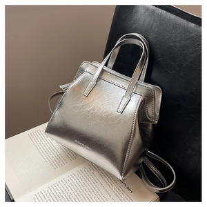 Detail of silver metallic tote bag with trapezoidal shape and dual handles on black leather