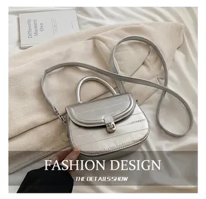 Detail of silver crocodile pattern saddle bag with metallic buckle on white fabric