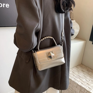 Sac bandoulière argenté avec poignée à perles et fermoir géométrique porté par un mannequin