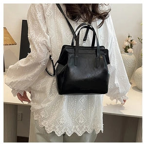 Model wearing a black matte leather backpack and handbag with a white lace shirt