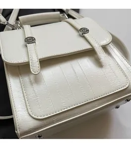 Detail of white textured shoulder bag with vertical stripe embossing and metal buckle