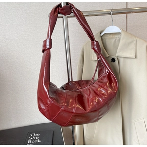 Detail of burgundy glossy leather hobo bag with quilted design and knotted shoulder strap