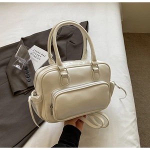 Detail of a creamy white Boston bag with outer zipper pocket on a white bedding background