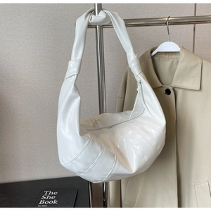 Detail of white glossy dumpling bag showing curved stitching and knotted strap design