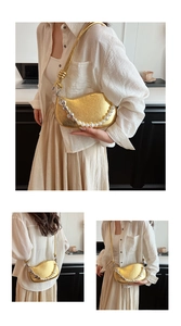 Detail view of gold pleated crescent bag with pearl and heart pendant metal chain strap