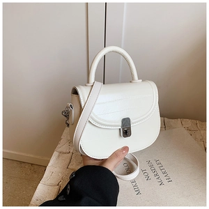 Close-up of white crocodile pattern saddle bag held by model against stone background