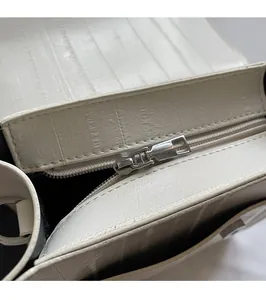 Detail of silver metal zipper and embossed faux leather texture on white handbag