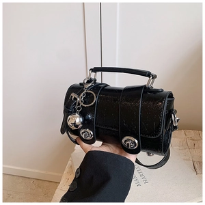 Détail du sac cylindrique noir en cuir verni craquelé avec ferrures argentées et charms