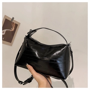 Detail of glossy black patent leather handbag with textured pleats and silver hardware