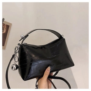 Close-up of black glossy trapezoid handbag with embossed texture and silver ball charm