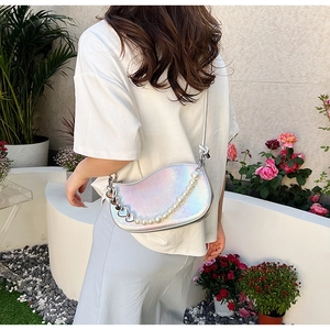Sac bandoulière demi-lune argenté irisé avec chaîne de perles dans un jardin extérieur