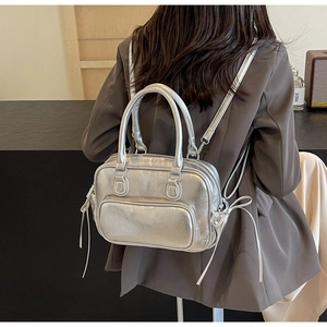Silver metallic backpack showing dual shoulder straps and zipper pockets on a model