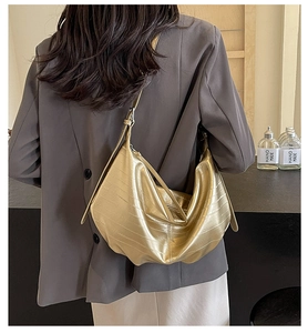 Detail of a gold metallic hobo bag with crocodile pattern worn on the shoulder