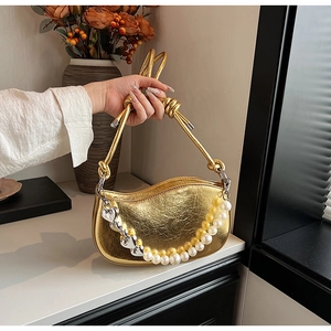 Detail of golden crescent handbag with pearl heart chain and metallic texture