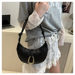 Detail of black woven leather crescent bag featuring a prominent gold horseshoe buckle