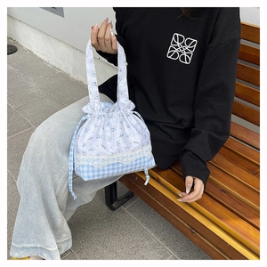 Detail of blue plaid and floral bucket bag with white lace trim in a sunny outdoor setting