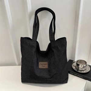 Grand sac cabas en toile noire avec écusson en cuir sur un bureau blanc moderne